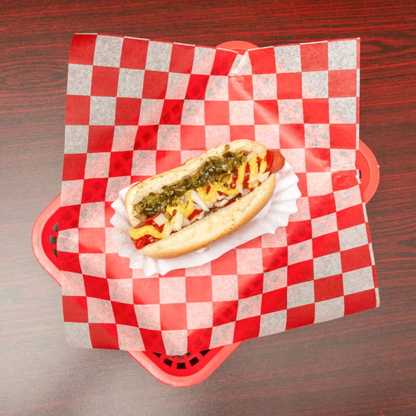 Hot dog with mustard, ketchup, relish, and onions in a red checkered basket.