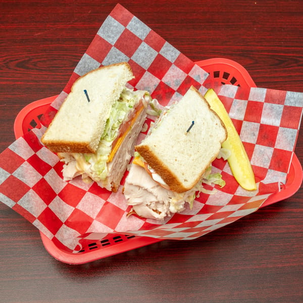 Turkey sandwich with lettuce, tomato, and cheese, cut in half, served with a pickle spear.