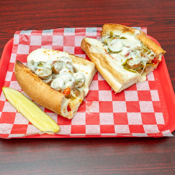 Two halves of a sausage and pepper sub sandwich with melted cheese and a pickle spear.