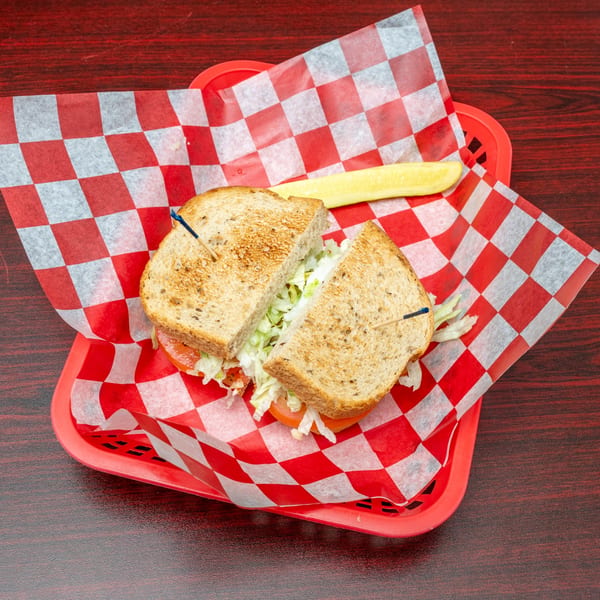 Toasted sandwich with lettuce and tomato, cut in half, served with a pickle spear in a red basket.