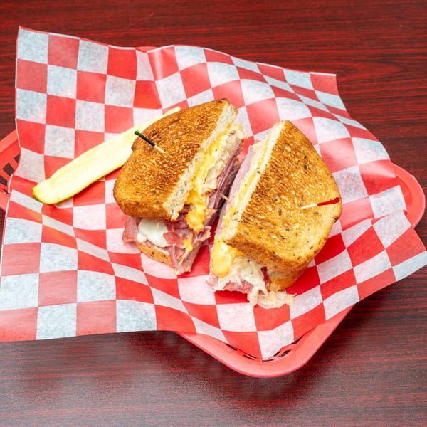 Reuben sandwich cut in half, with melted cheese and sauerkraut, served with a pickle spear.