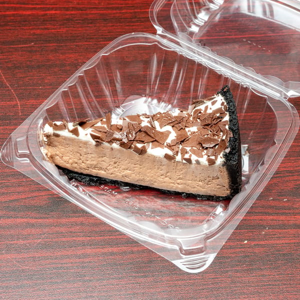 Slice of chocolate cheesecake with whipped cream and chocolate shavings in a clear plastic container.