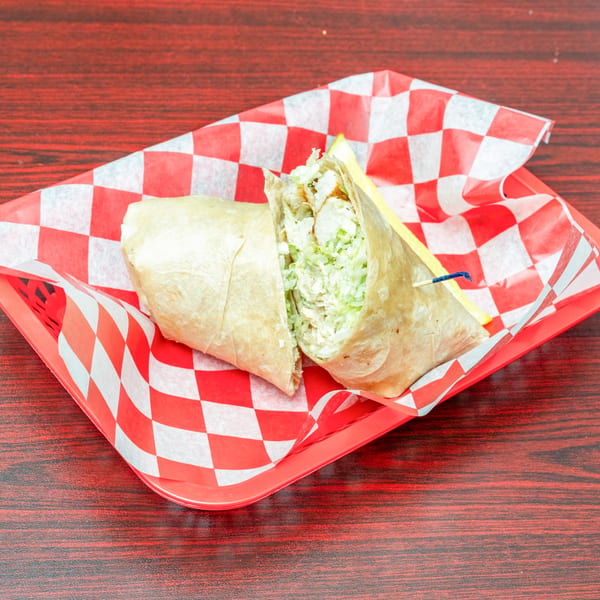 Chicken Caesar wrap, cut in half, served in a red basket with checkered paper lining.