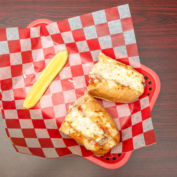 Two cheesy breadsticks and a pickle spear in a red basket with checkered paper.